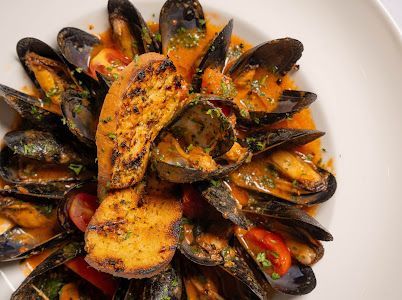 Mussels in orange sauce with toasted bread on a white plate.
