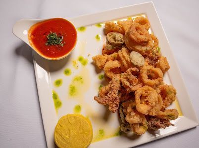 Fried calamari with red dipping sauce and lemon slice on a white plate.