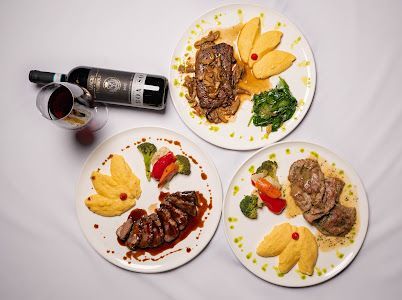 Three plates with steak, polenta, vegetables, and a bottle of wine with a glass.