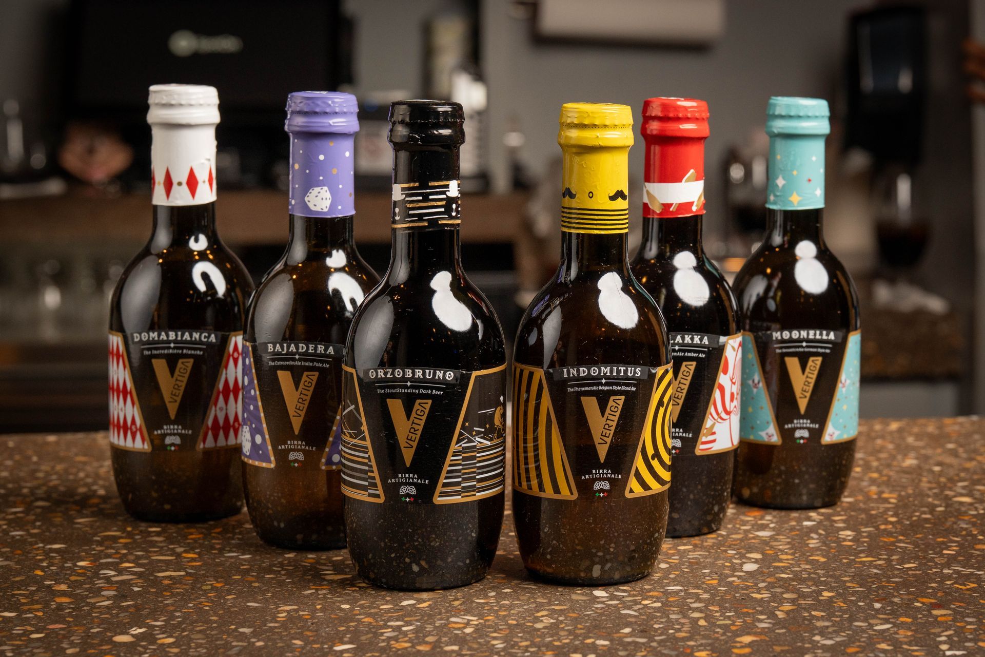 Seven dark, ornate wine bottles with colorful, patterned tops arranged on a textured surface.