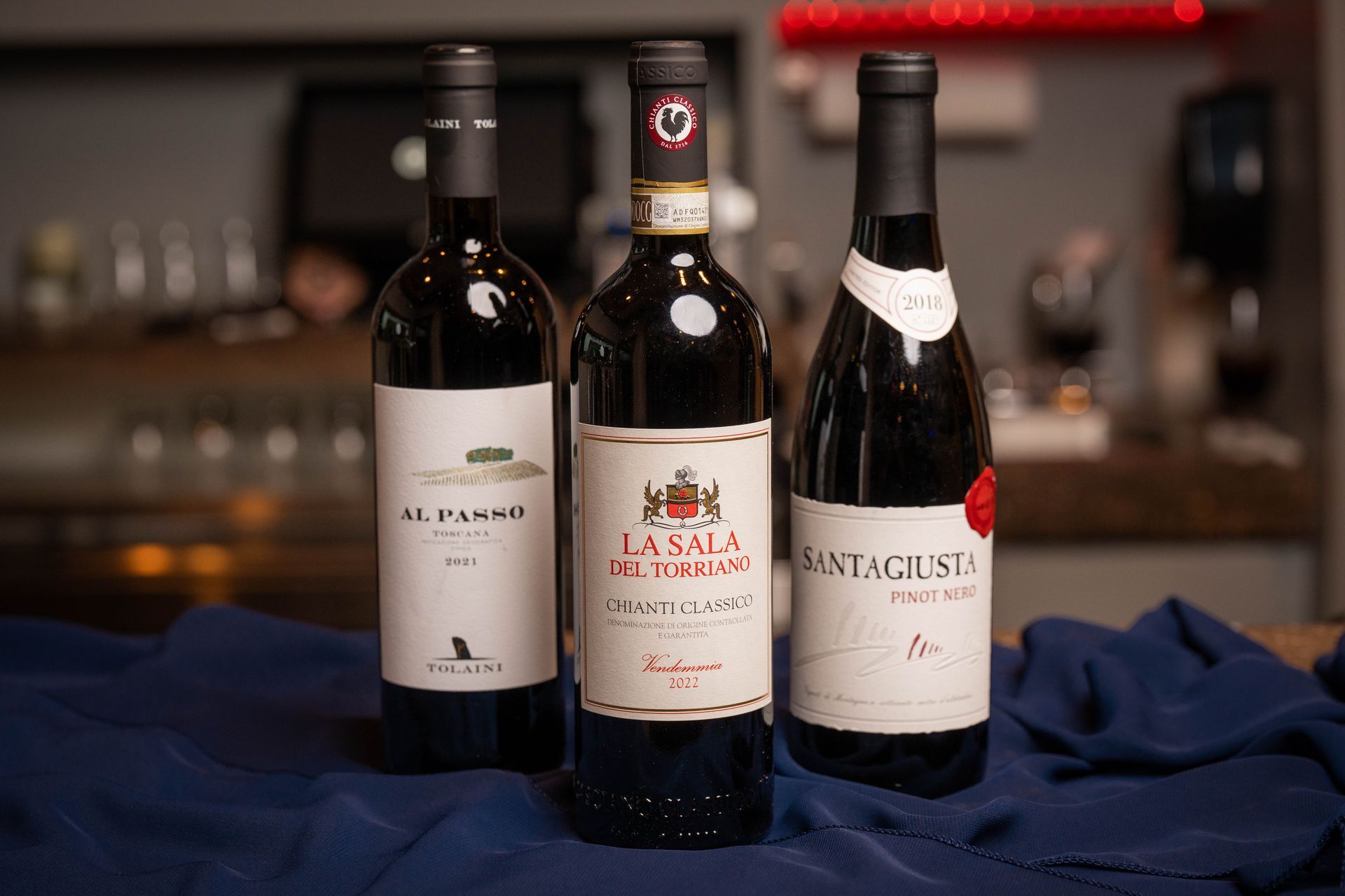 Three bottles of red wine on a blue cloth. The bottles have labels with names like 