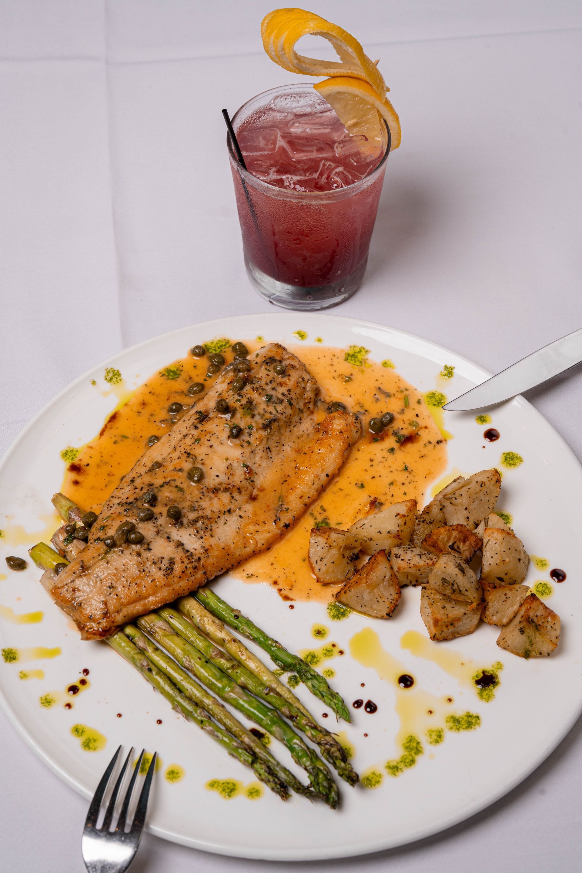 Plate of fish with asparagus and potatoes, plus a cocktail with a lemon peel garnish.