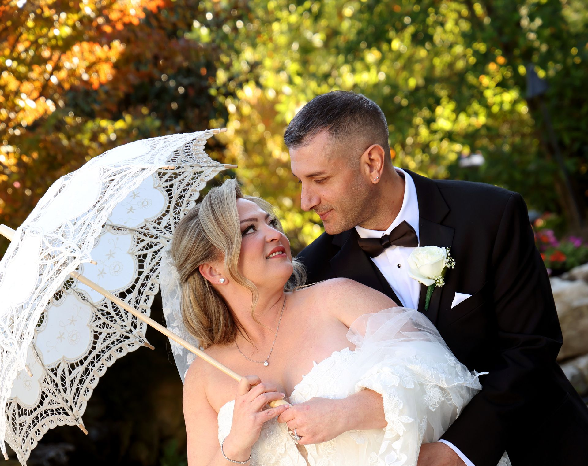 Bride holding vintage lace parasol as groom leans in