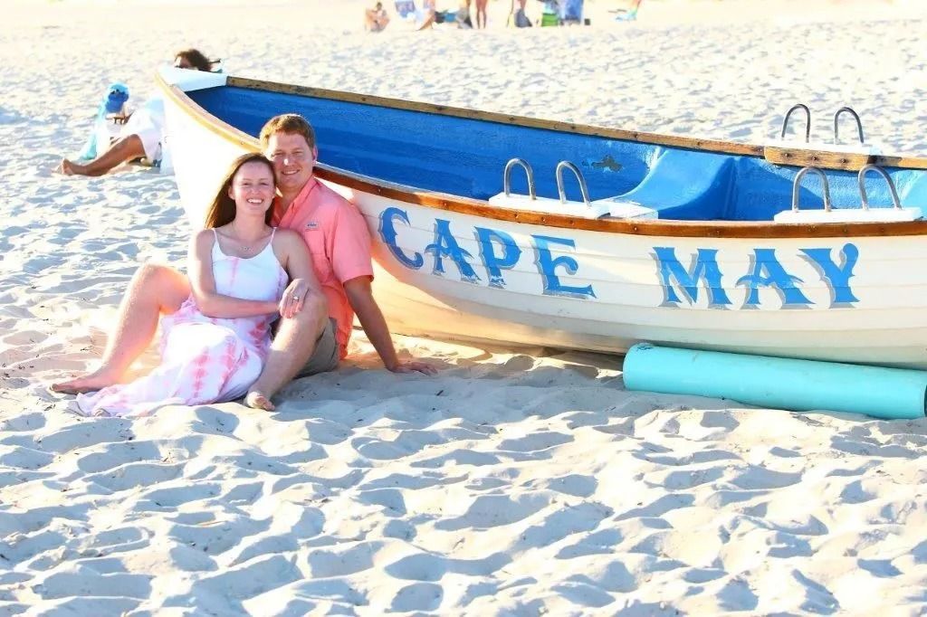 Couple sitting on beach next to a boat that says 