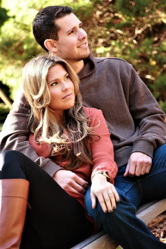 Couple sitting outdoors, man has arm around woman. They are gazing upward, sunlight.