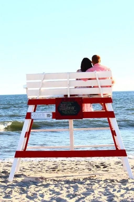 Couple sits on a lifeguard stand overlooking the ocean, red and white stand.
