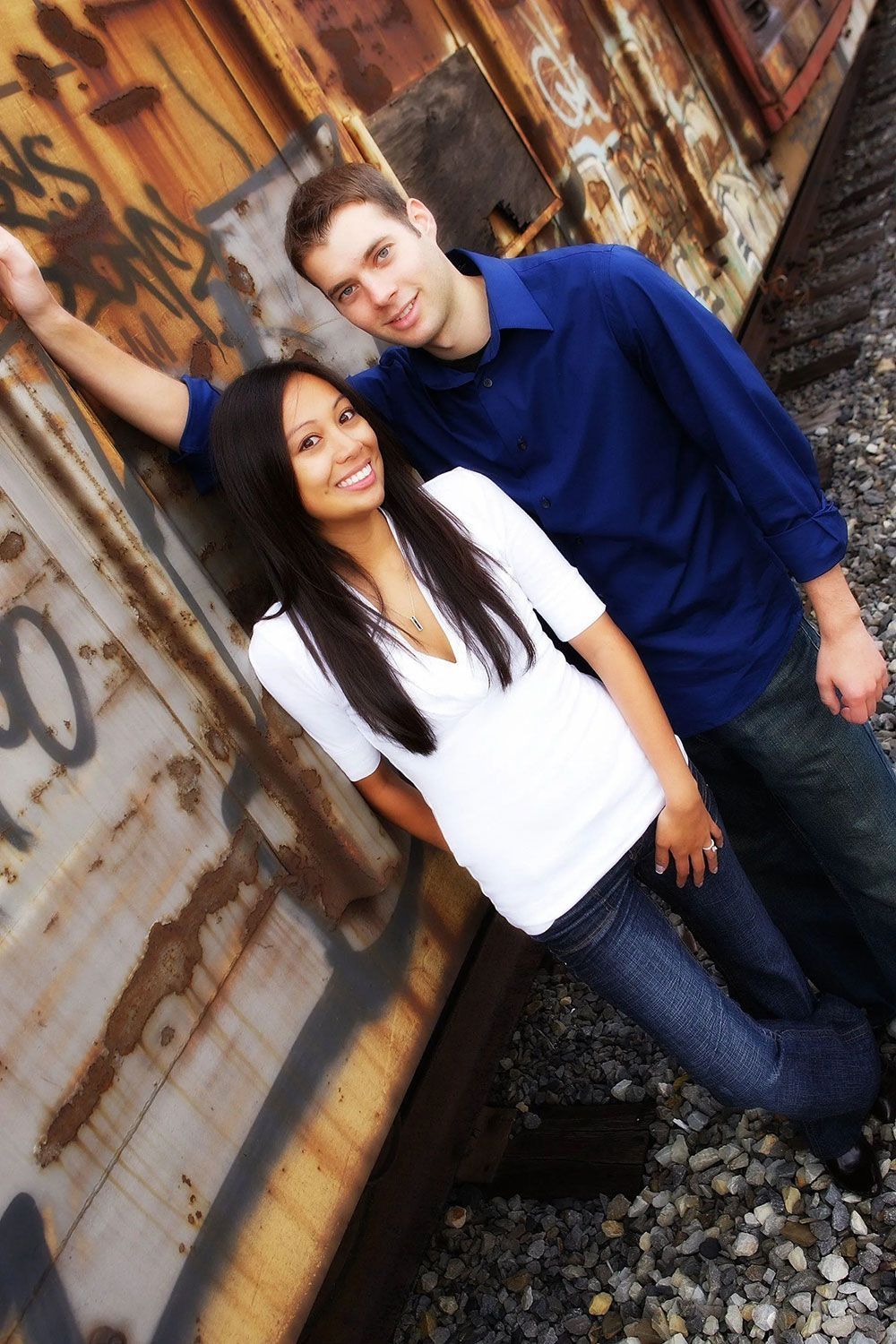 Couple leaning against a graffiti-covered train car; woman smiles, man looks at the camera.