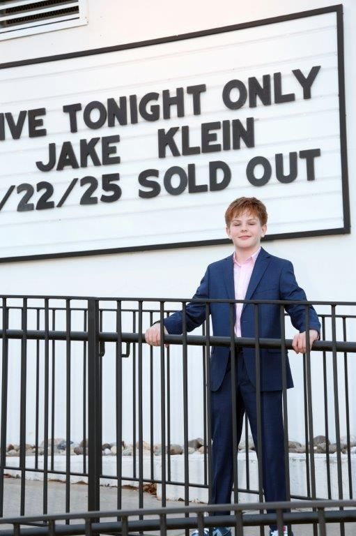 Boy in blue suit stands outside venue with sold-out sign for 