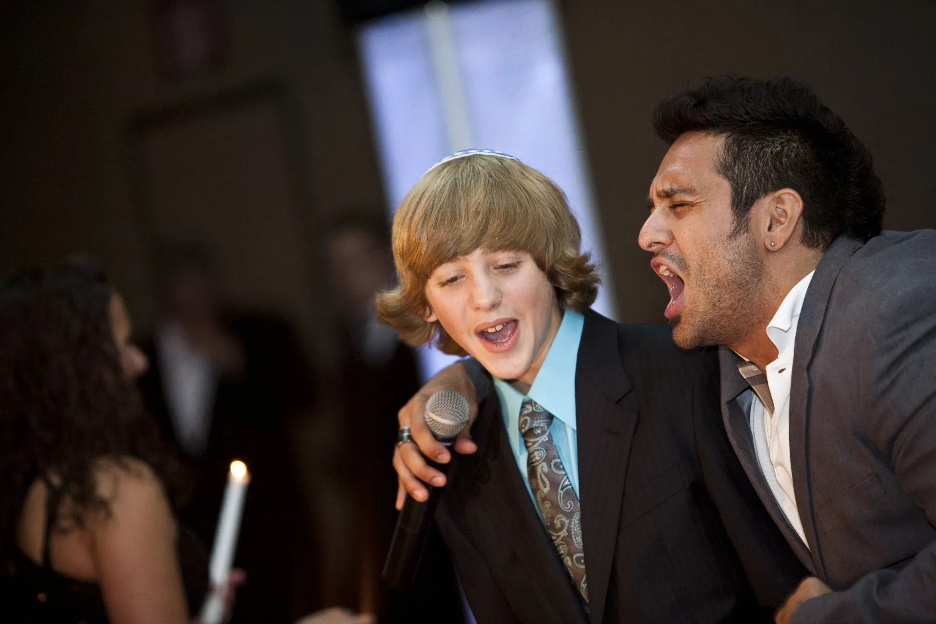 Boy singing into microphone with man, both in suits, at an event.