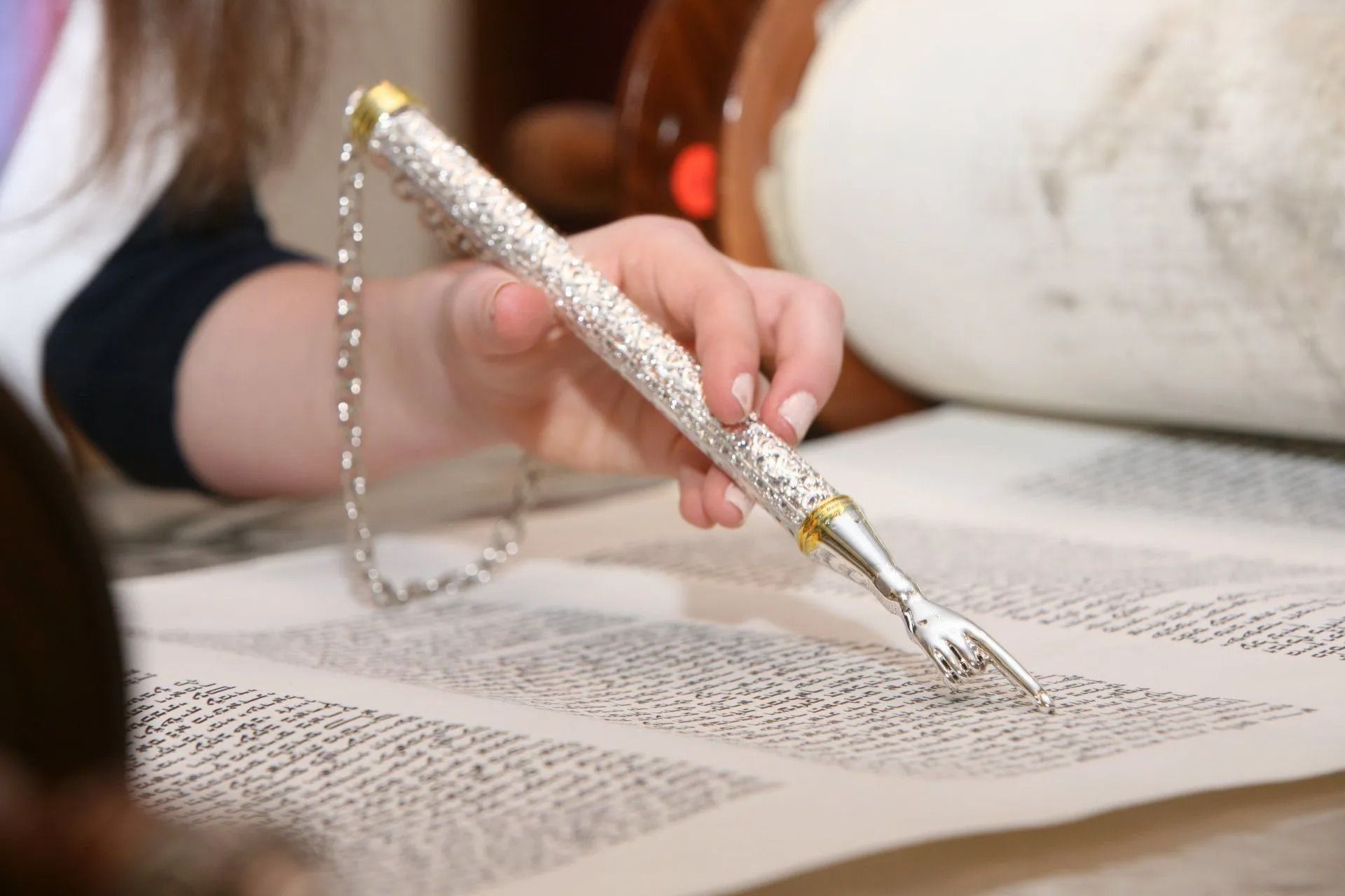 Hand holding a silver pointer, reading a Torah scroll.