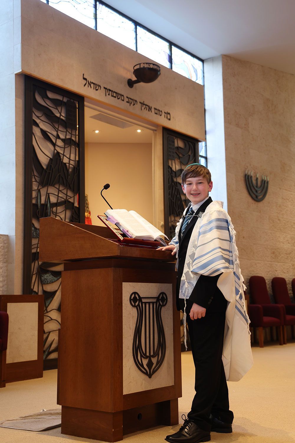 Boy in a prayer shawl at a podium in a synagogue.