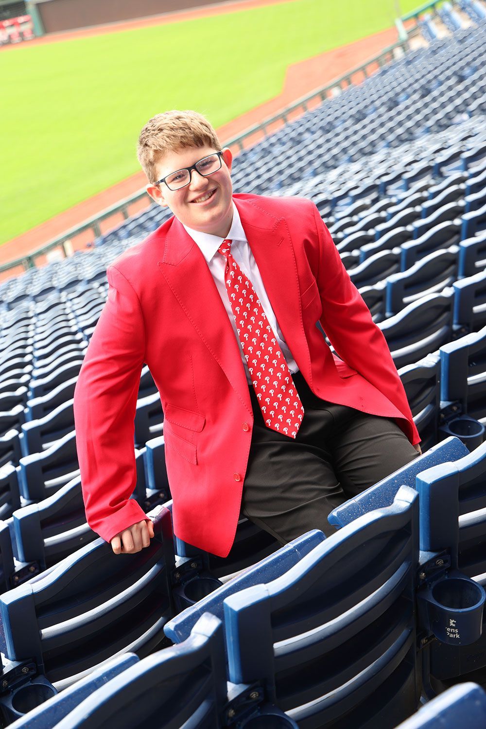 Person in a red blazer and tie, smiling, posed in stadium seating.