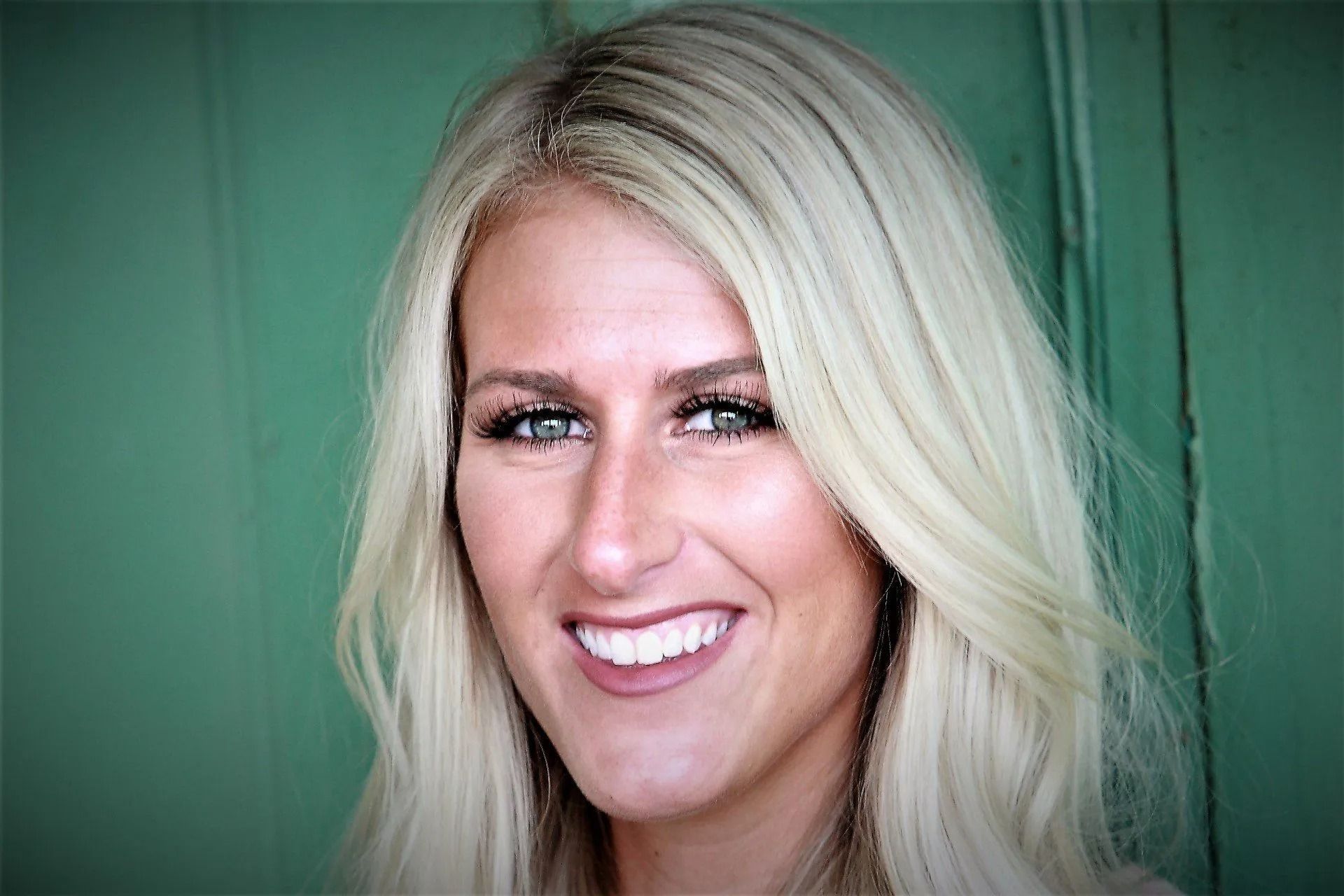 Blonde woman smiles, facing forward, against a green background.