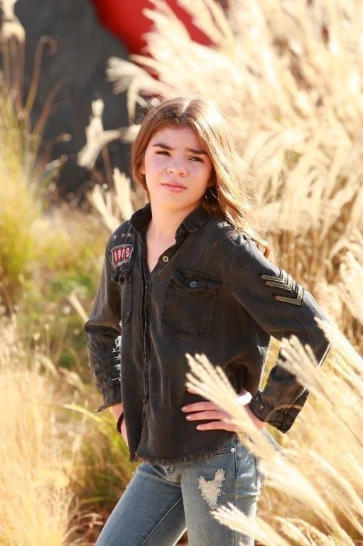 Young person in black shirt and ripped jeans poses in tall, golden grass.