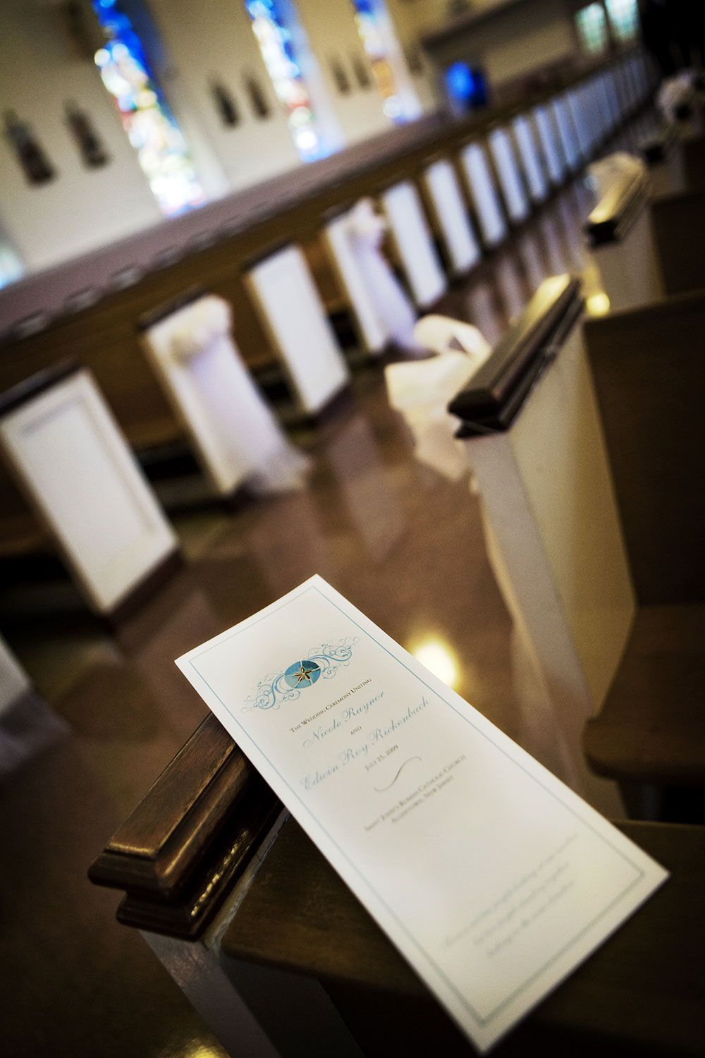 Wedding program on pew in church. Rows of wooden pews leading to a blurred background with stained glass.