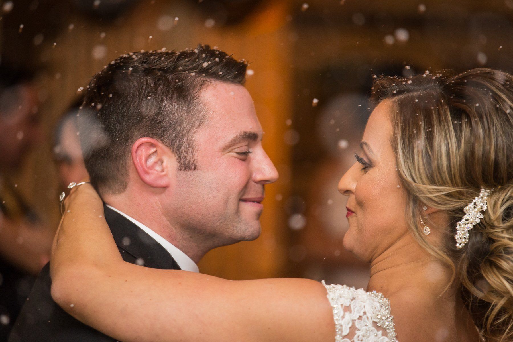 Bride and groom dancing at a wedding, snow falling, smiling, embracing.