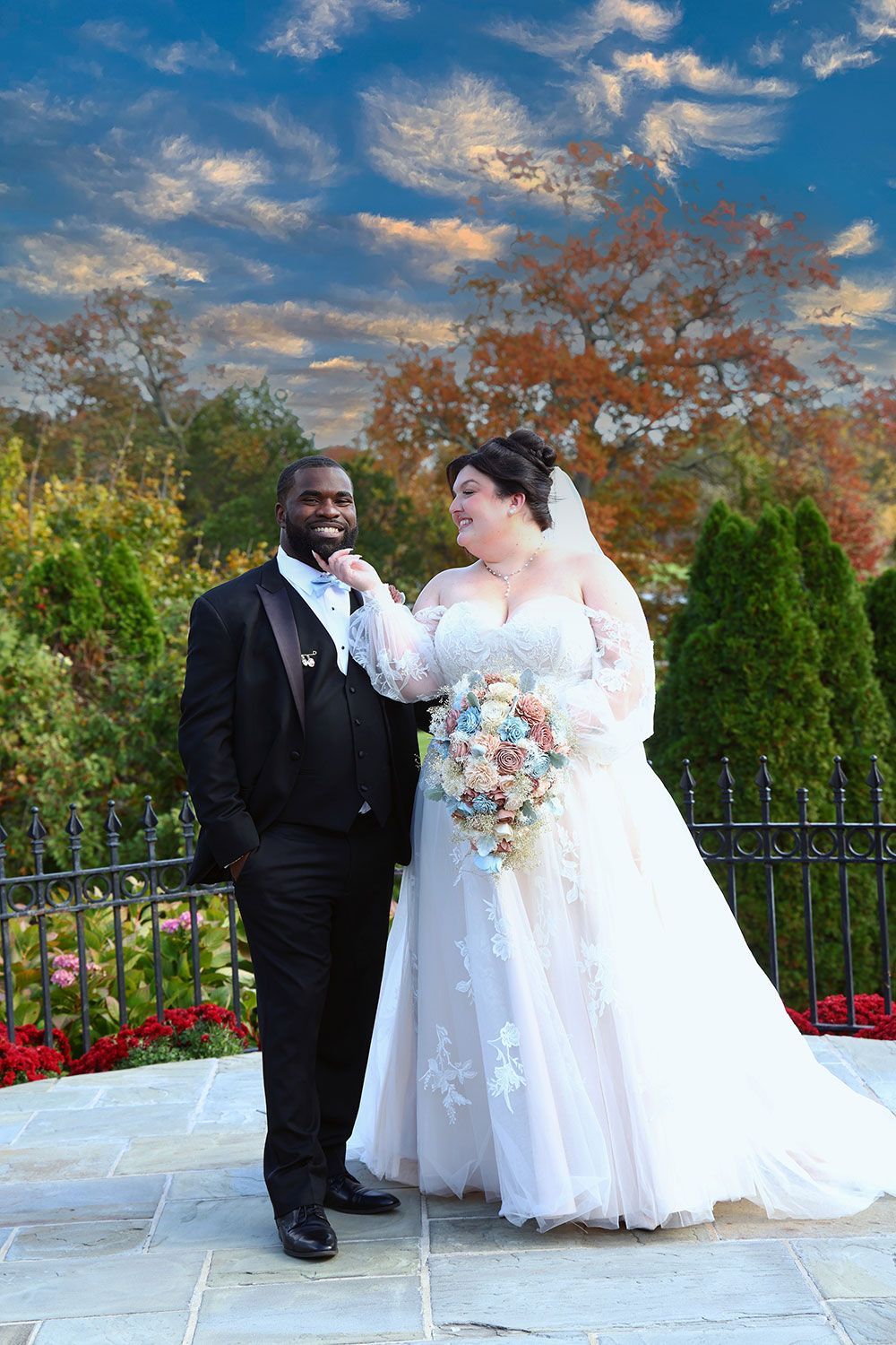 Bride in white dress touches groom's chin; autumn wedding photo outdoors.