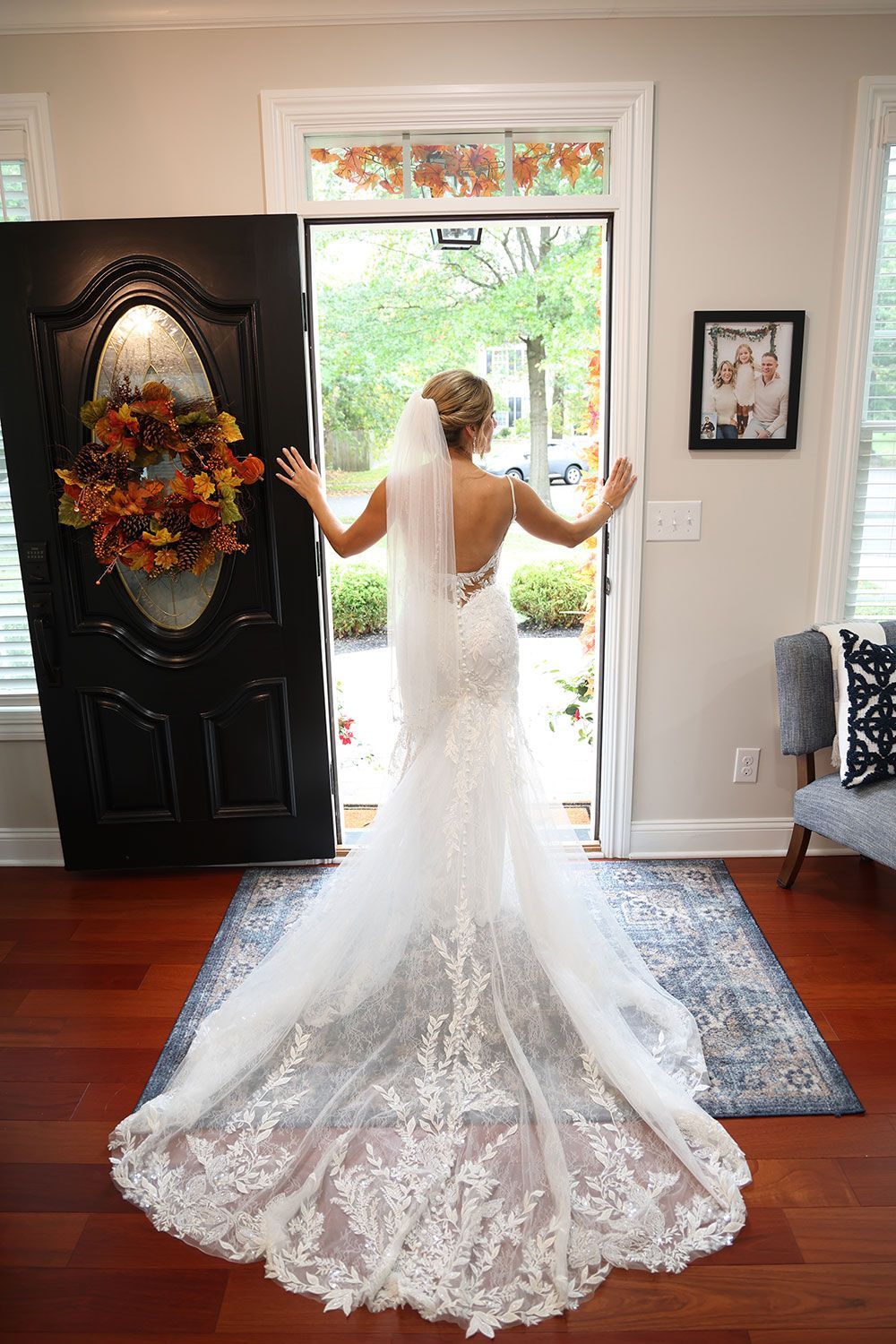 Bride in wedding dress, standing in doorway, arms outstretched, looking outside.