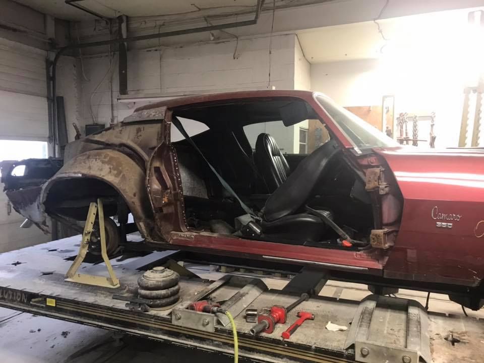 A classic maroon car body undergoing restoration in a garage. The interior is accessible.