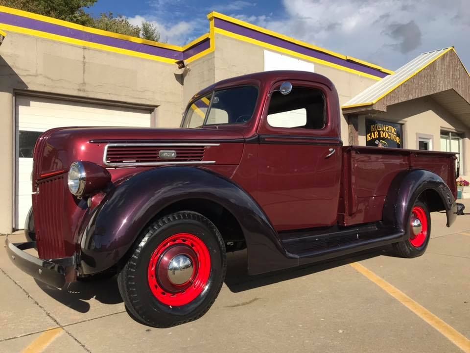 Burgundy vintage pickup truck with red wheel rims parked outside a building.