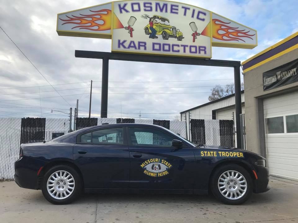 Dark blue State Trooper car parked under a