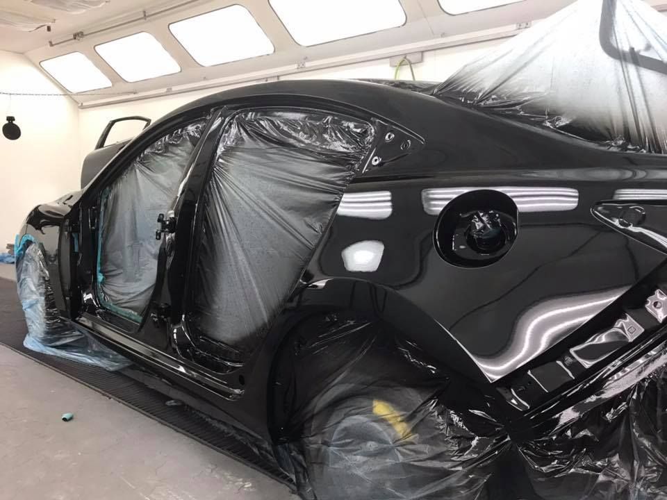 Black car partially covered in plastic for painting in a spray booth.