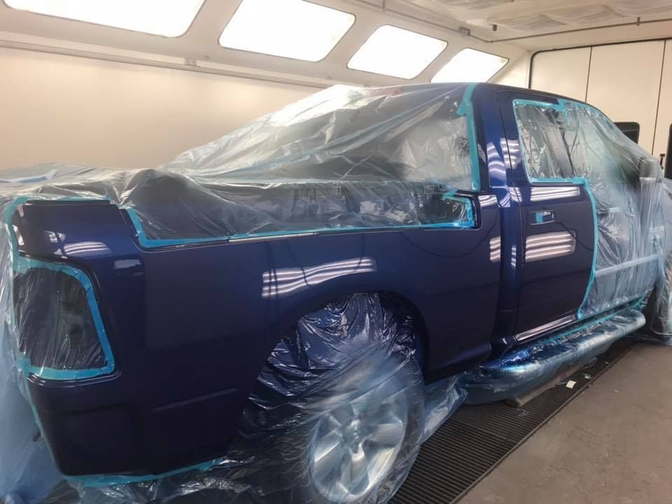 Blue pickup truck in a paint booth, covered in plastic sheeting, ready for painting.