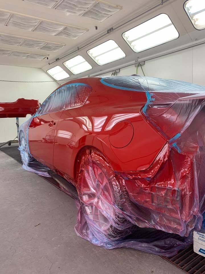 Red car partially covered in plastic in a paint booth, ready for painting.