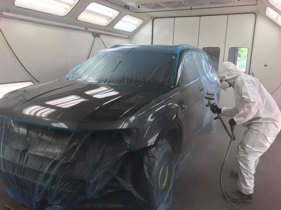 A person in protective gear spray-painting a car inside a paint booth.