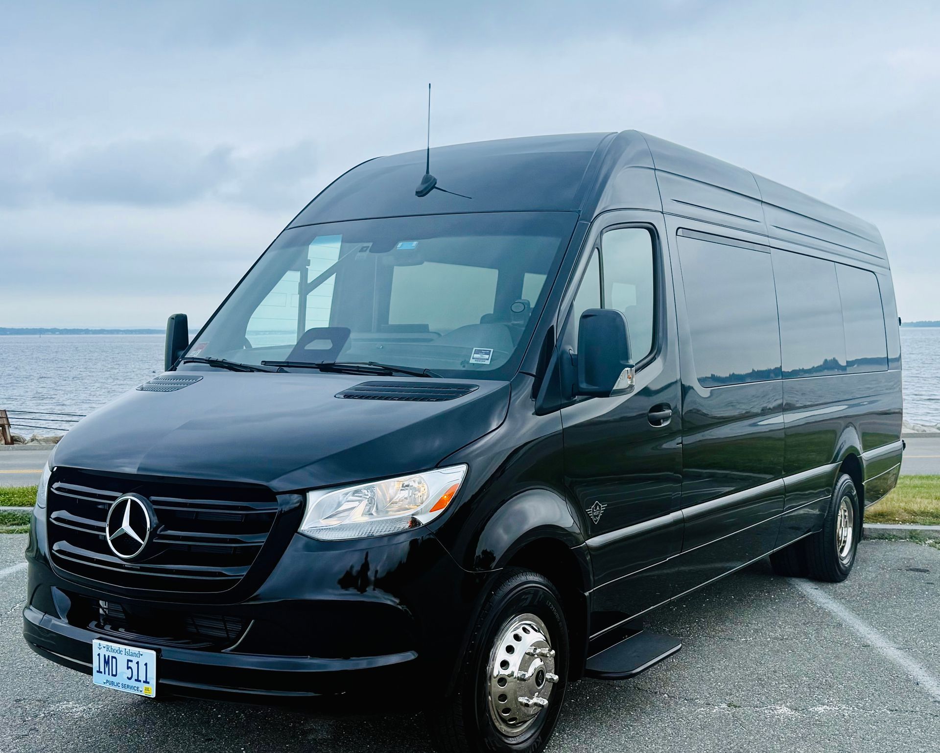 Black Mercedes Sprinter van parked by the water on a cloudy day.