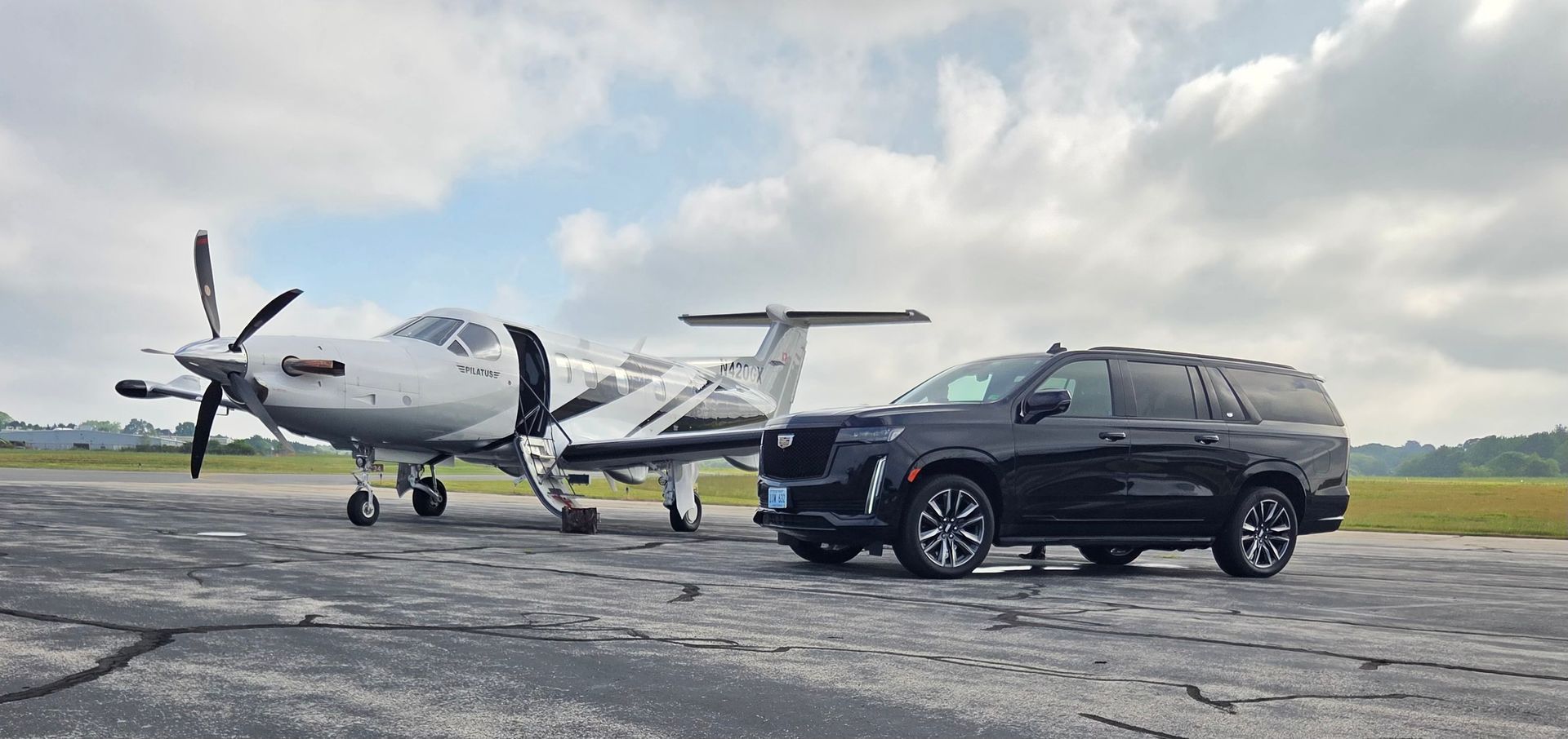 A black SUV parked next to a small airplane on a runway under a cloudy sky.