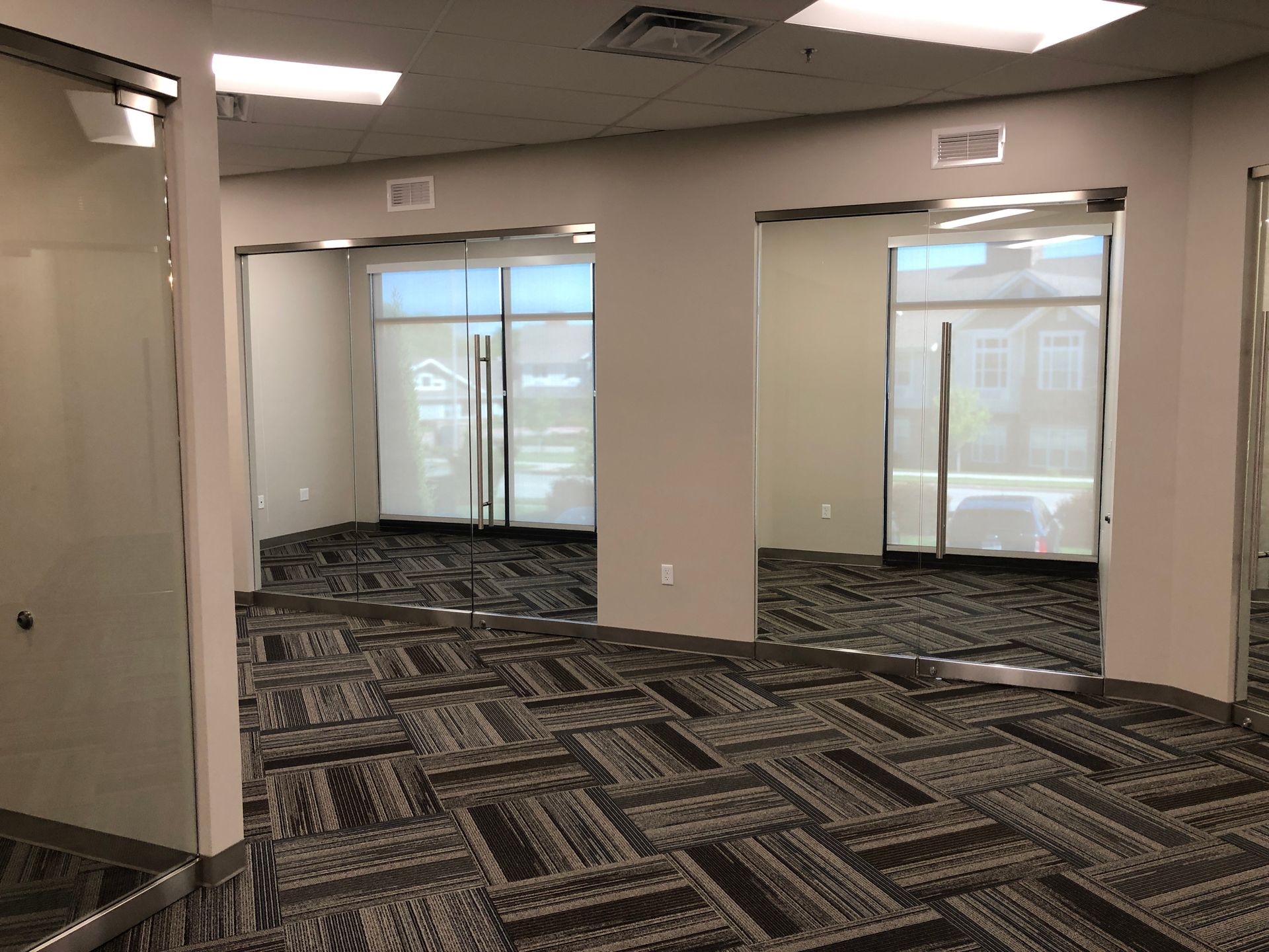 A large empty room with a carpeted floor and glass doors.