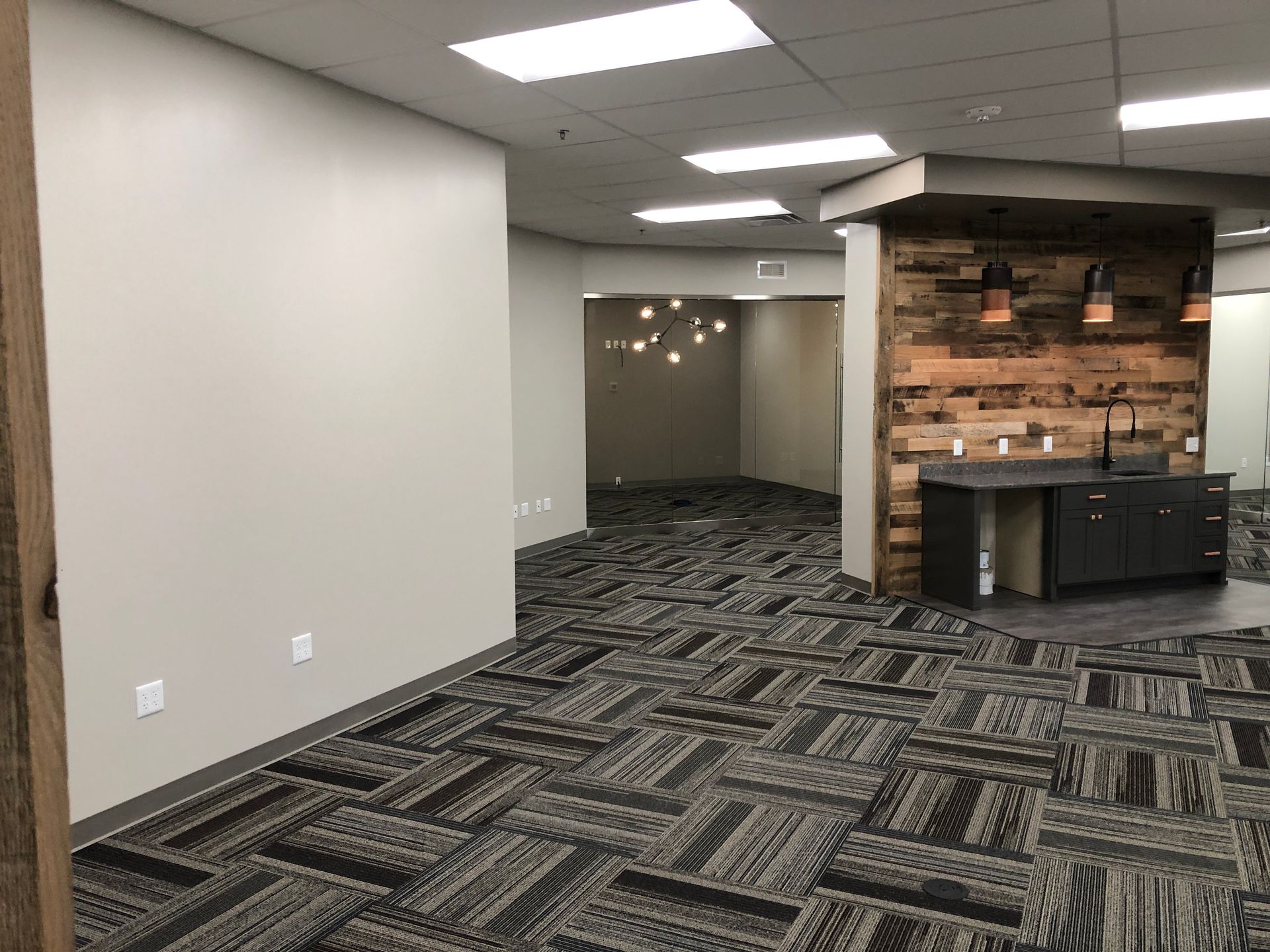 A large empty room with a carpeted floor and a wooden wall.