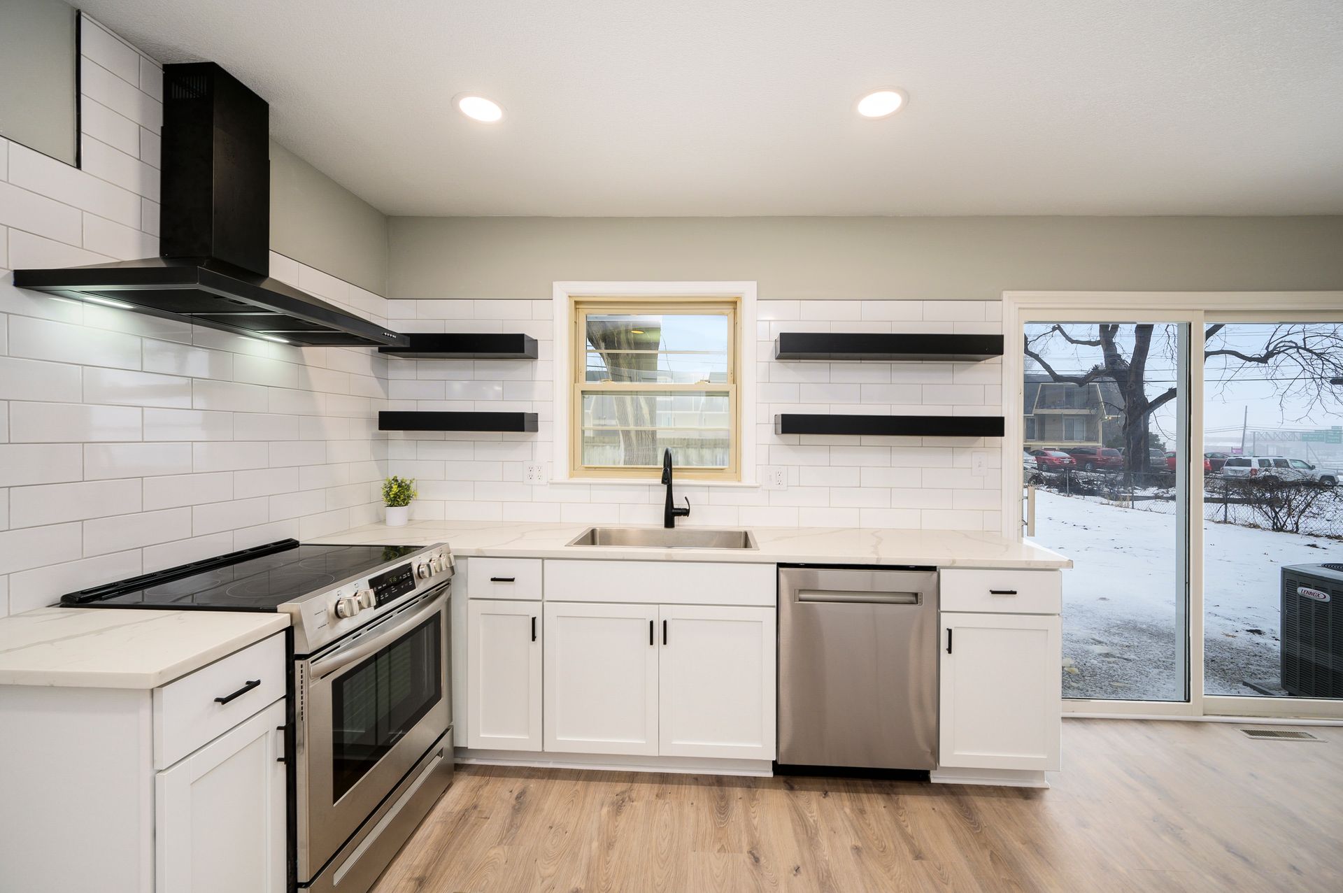 A kitchen with white cabinets , stainless steel appliances , a sink and a window.