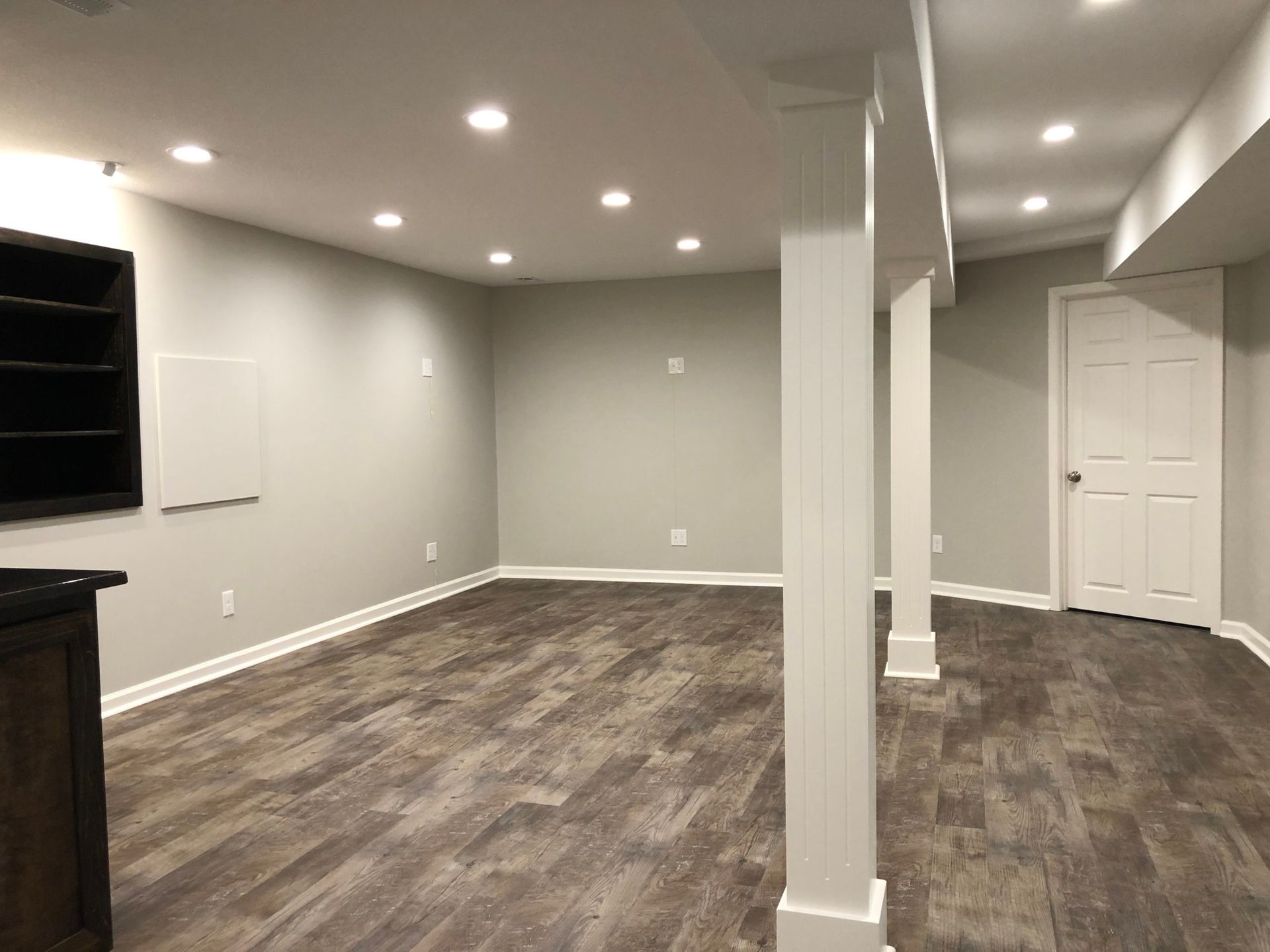 An empty basement with hardwood floors and white pillars.