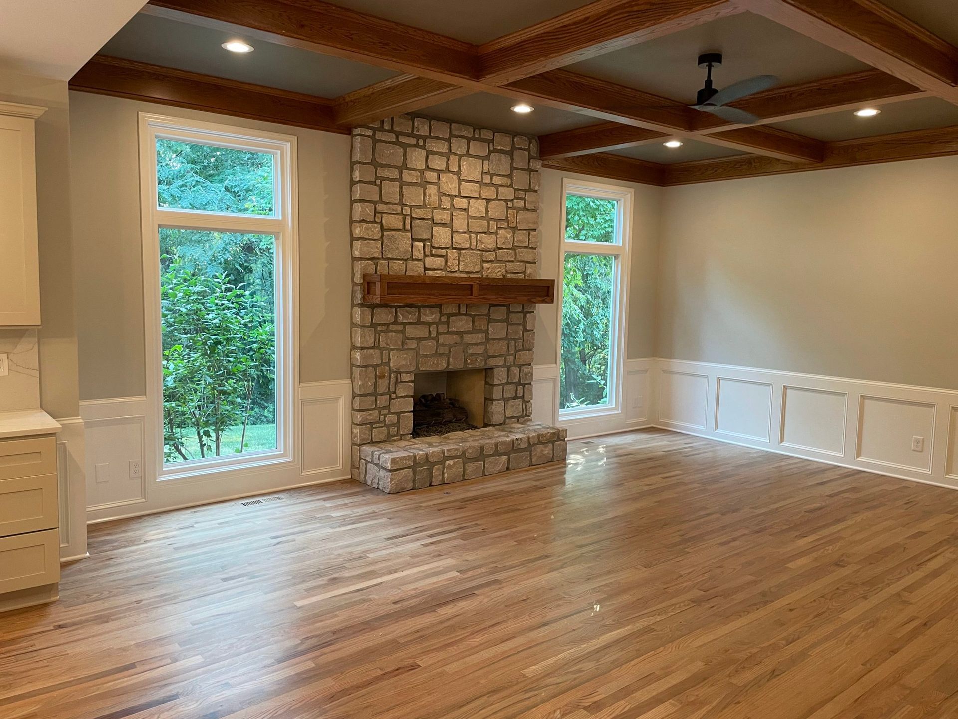 An empty living room with hardwood floors and a stone fireplace.