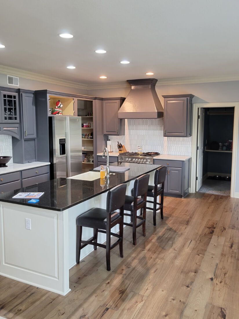 A kitchen with gray cabinets , black counter tops , stainless steel appliances , and wooden floors.