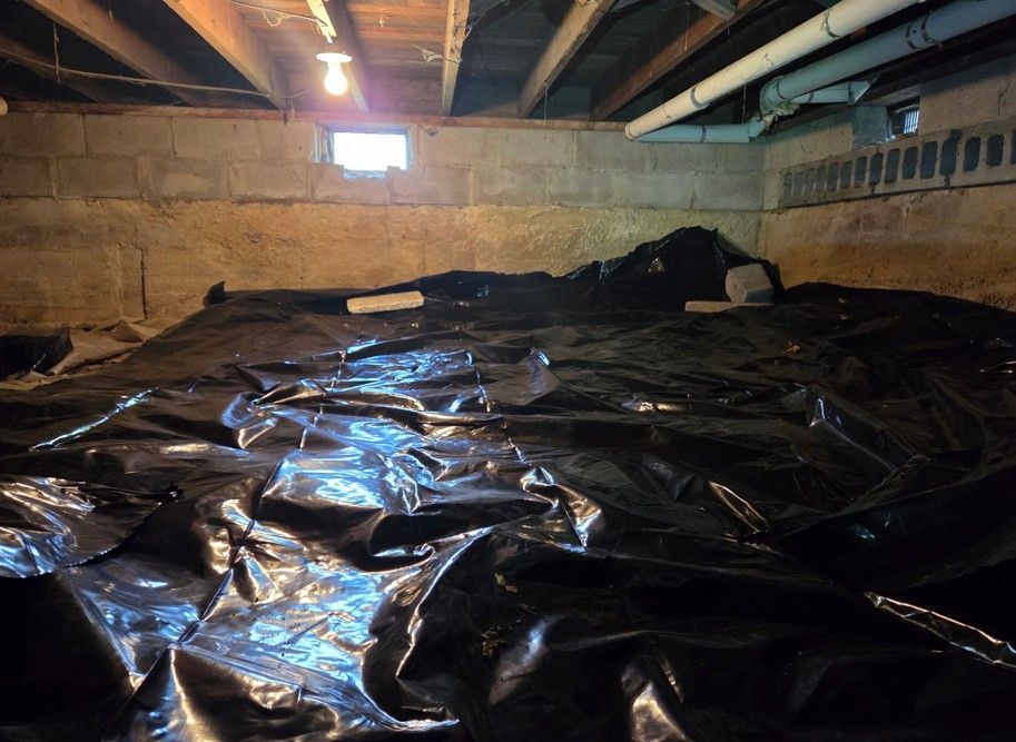 Basement with large black plastic sheeting covering the floor under exposed beams and a small window.