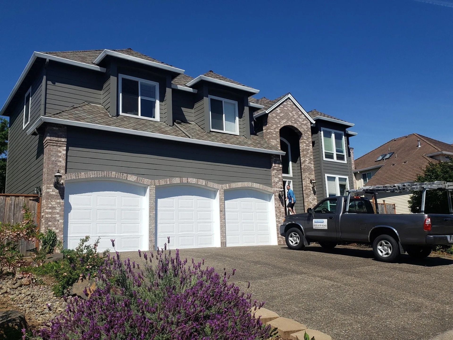 Two-story gray house with a brick facade and a three-car garage, with a pickup truck parked in the driveway.