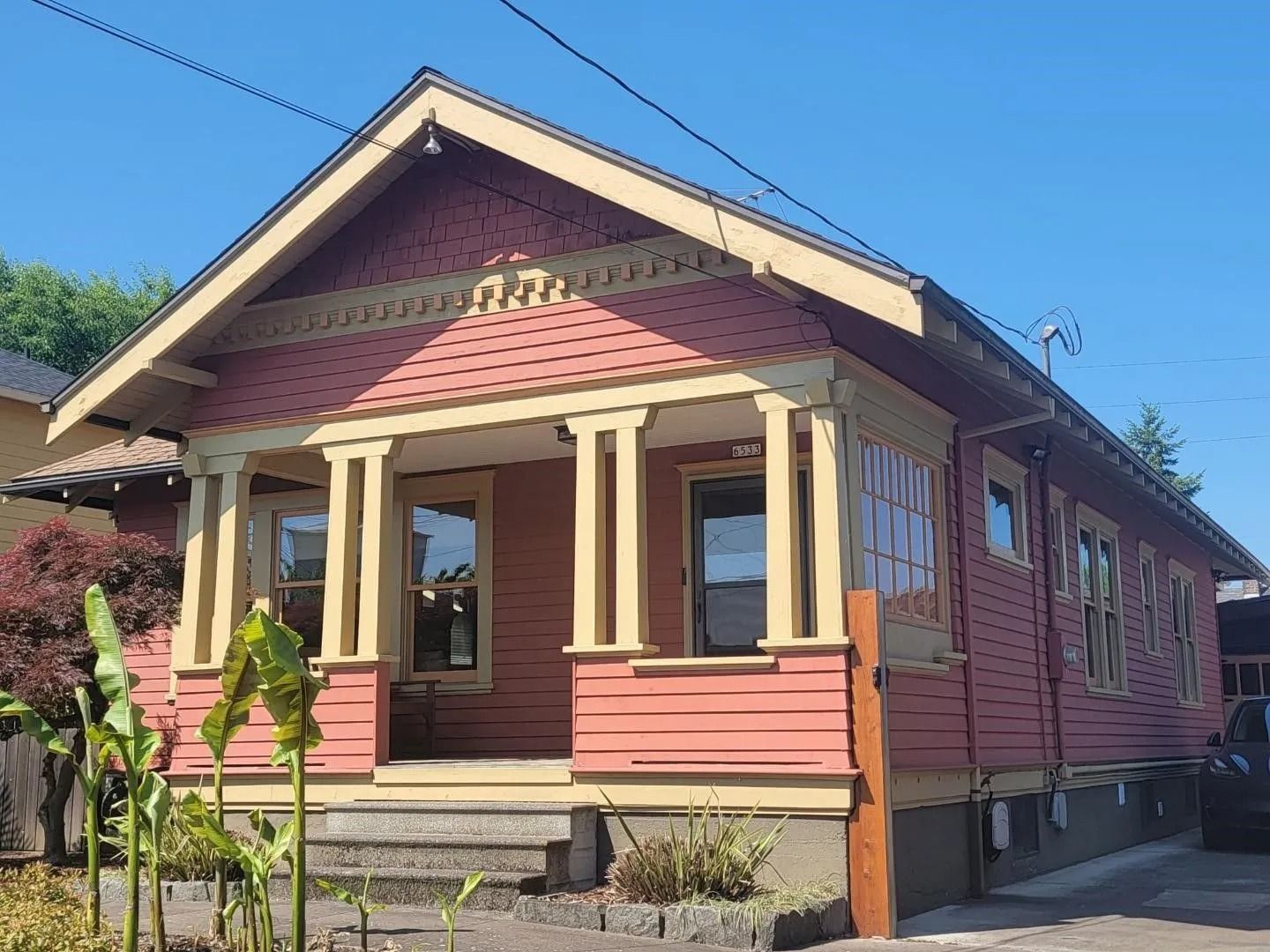 A pink, one-story bungalow with a columned front porch, set under a clear blue sky.
