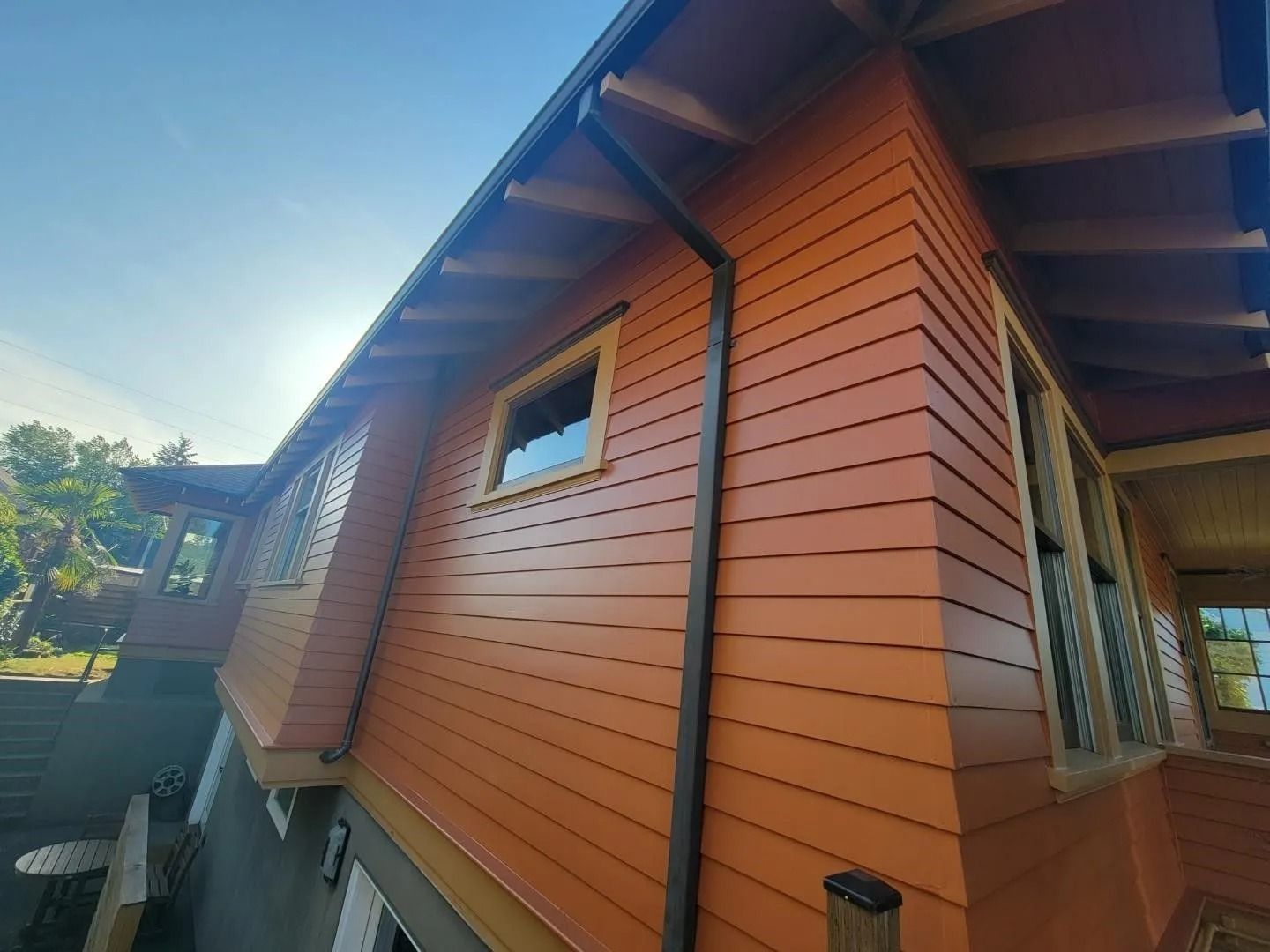 An orange wooden house exterior with horizontal siding, dark brown gutters, and windows against a sunny blue sky.