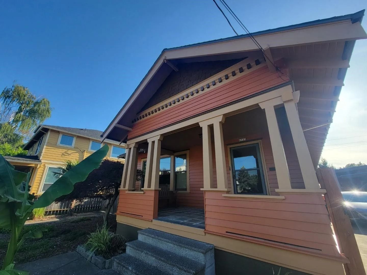 A low-angle view of a salmon-colored bungalow with a covered porch featuring decorative columns and wooden siding.