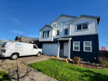 A white work van parked on a driveway in front of a two-story house with dark blue lower siding and white upper siding.