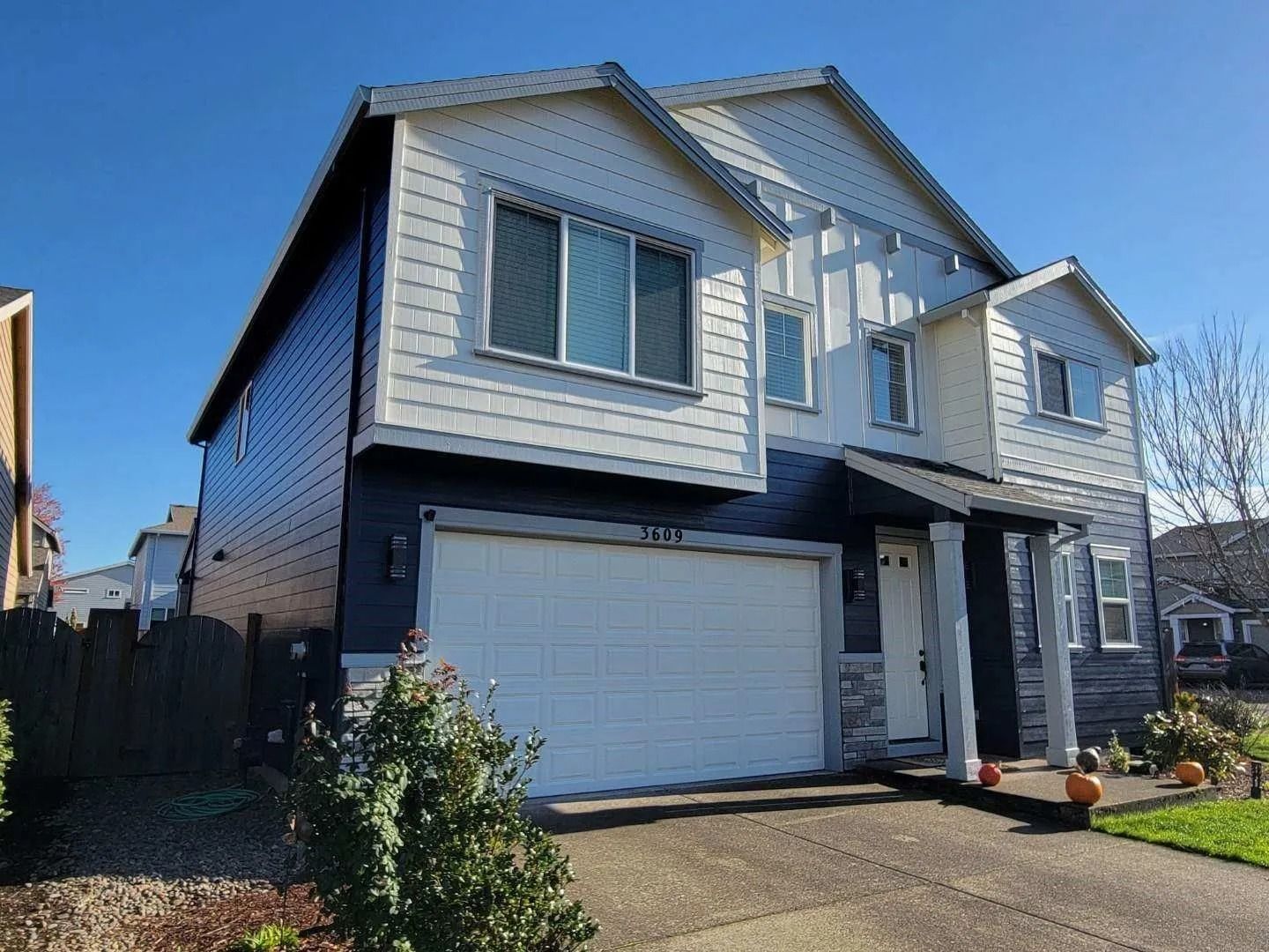 A two-story house with dark blue siding, white trim, a white garage, and a light stone facade on a sunny day.