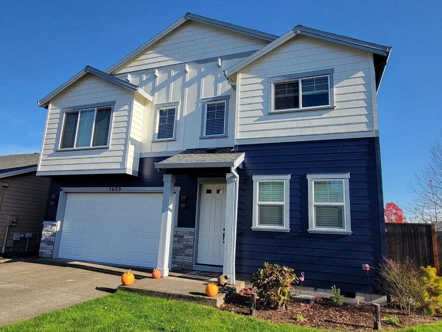 Two-story house with a white garage and upper level, dark blue lower level, and stone accents under a clear blue sky.