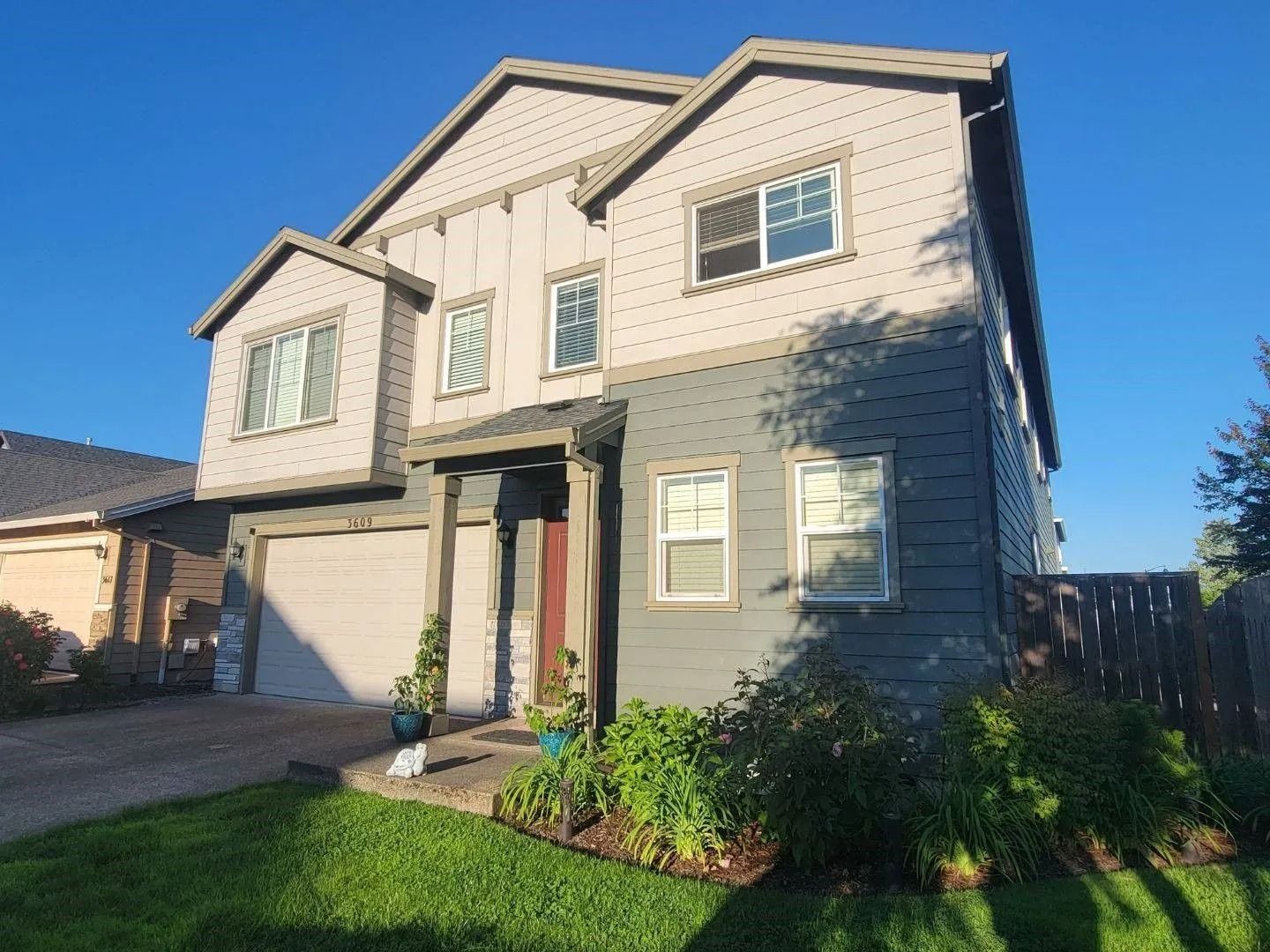 Two-story suburban house with light siding on top, gray siding on the bottom, a garage, and a front porch.