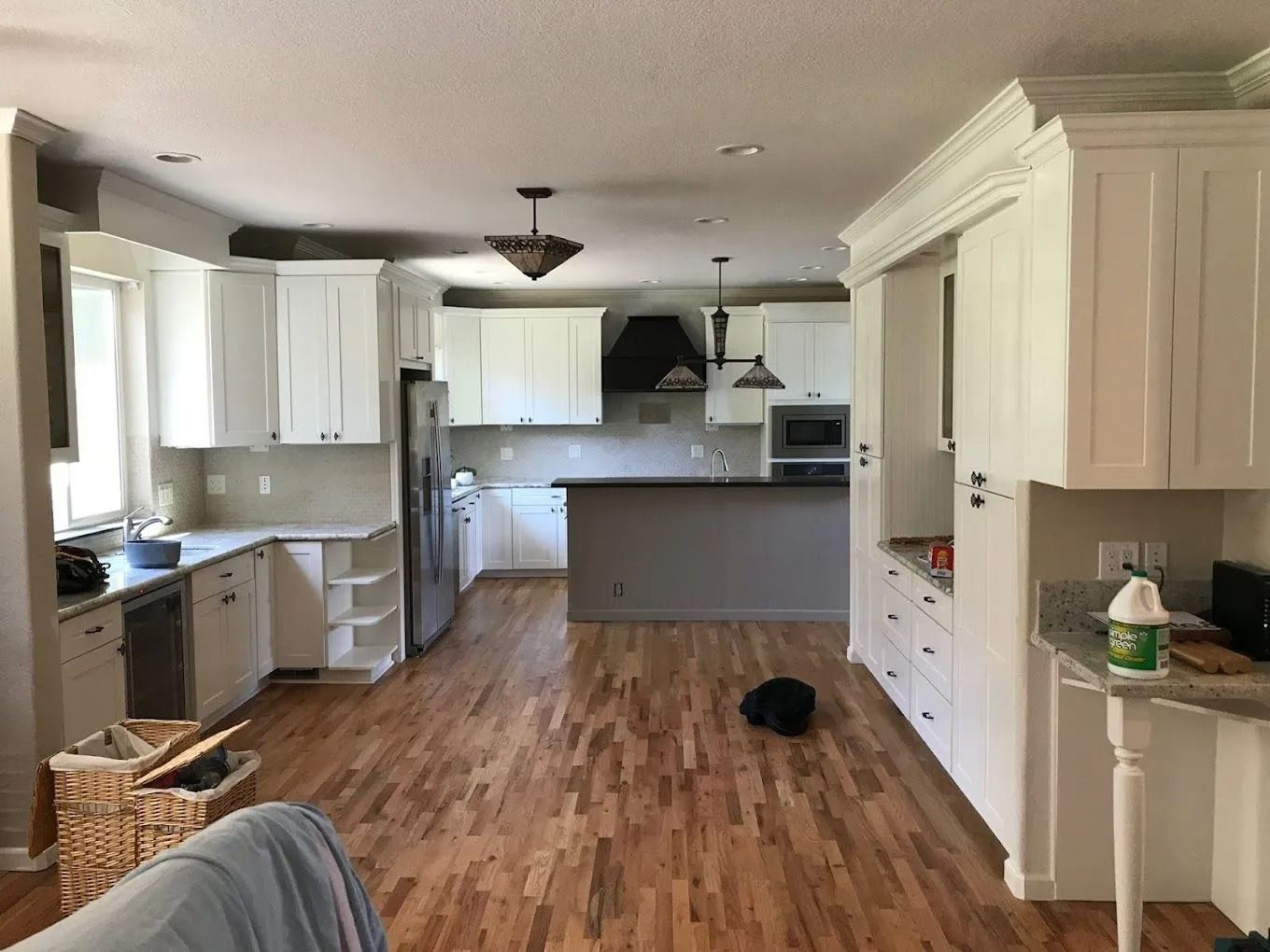 A bright, open-concept kitchen featuring white cabinets, wood flooring, and a large central island.