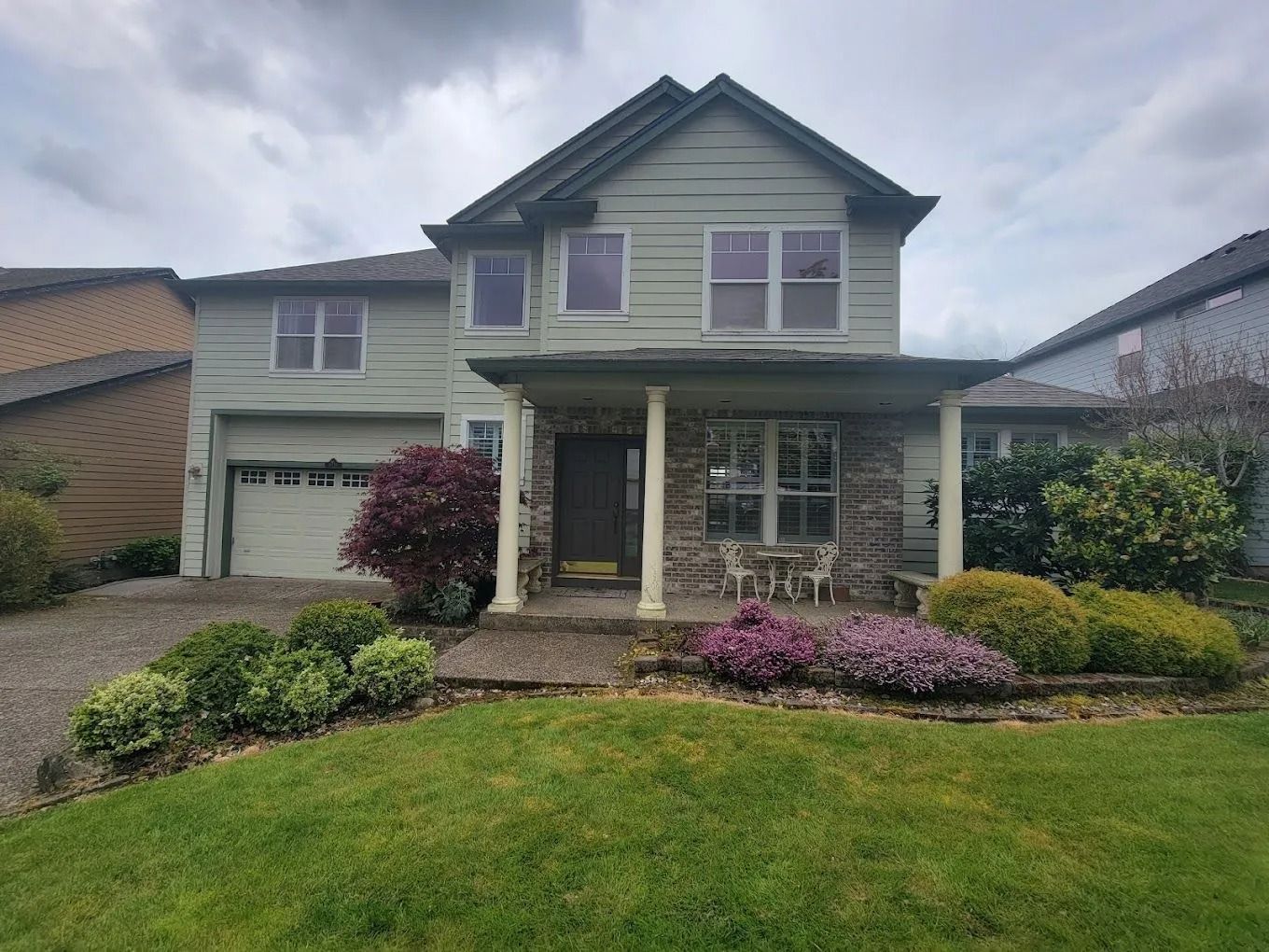 Two-story house with light green siding, a stone-accented front porch, an attached garage, and a landscaped front yard.