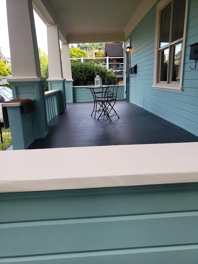A covered front porch with light blue siding, white pillars, a dark gray floor, and a small table with two chairs.