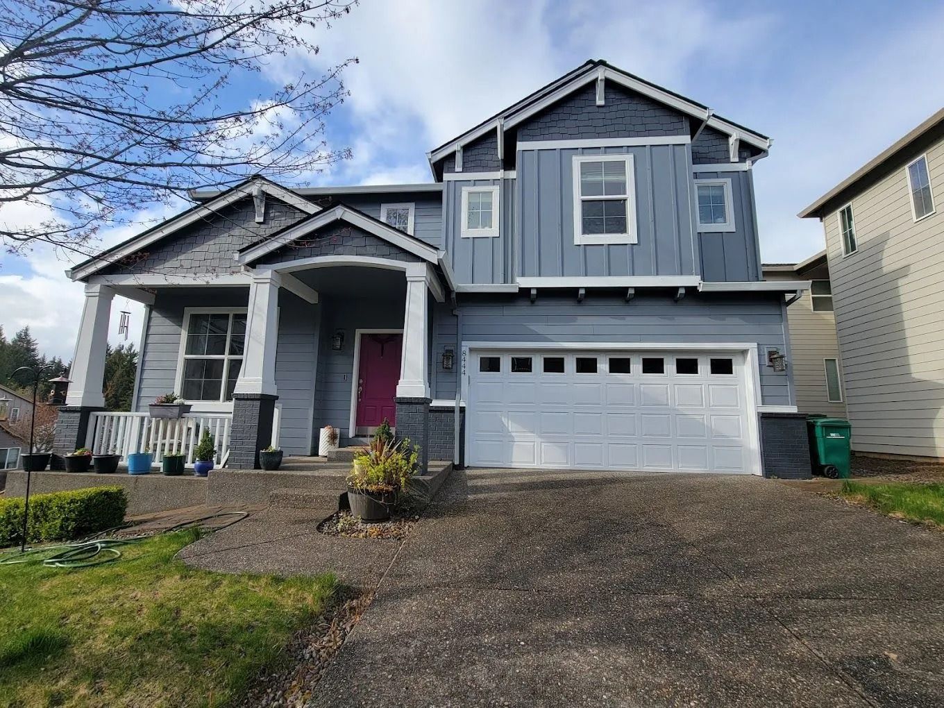 A two-story blue house with white trim, a white garage door, and a bright pink front door under a small porch.